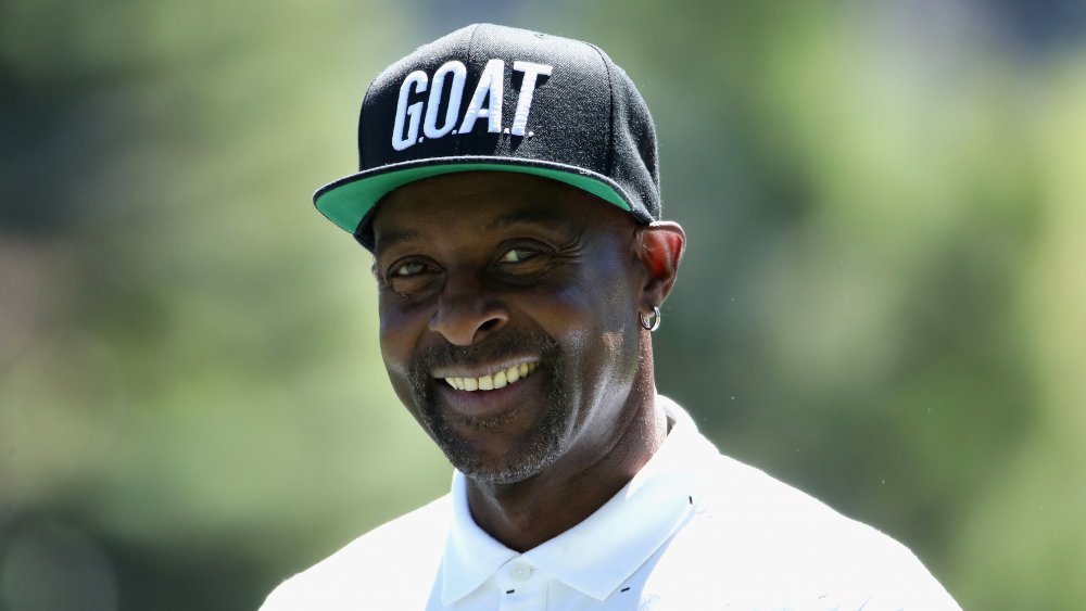 Jerry Rice smiling in a white polo shirt and black GOAT hat