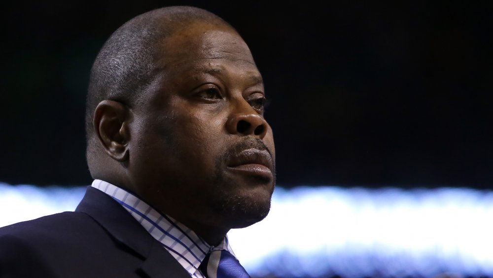 Patrick Ewing in a blue blazer and checkered shirt, looking off to the side with a serious expression