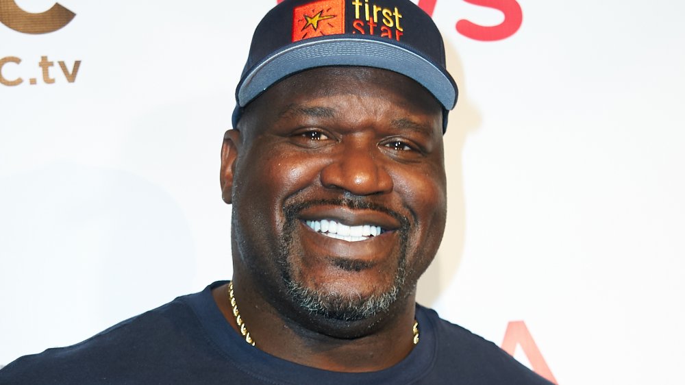 Shaquille O'Neal smiling in a blue t-shirt and hat
