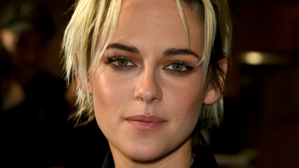 Kristen Stewart in a black outfit, with short blonde hair and small smile at a premiere
