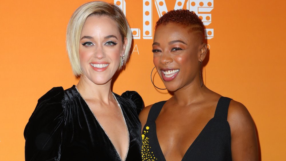 Lauren Morelli in a black velvet dress, Samira Wiley in a black, yellow-accented dress, smiling at Trevor Live