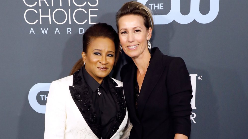 Wanda Sykes in a white-and-black suit with wife Alex Niedbalski, smiling and posing together at the Critics Choice Awards