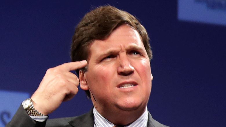 Tucker Carlson with finger to head, squinting