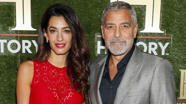 Amal Clooney wearing red dress with George Clooney