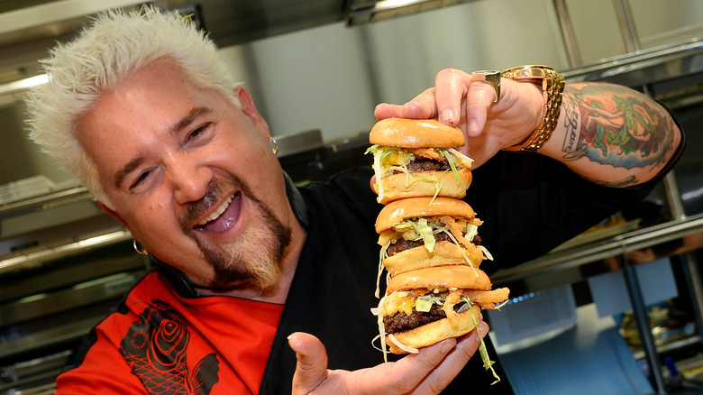 Guy Fieri holding three stacked burgers