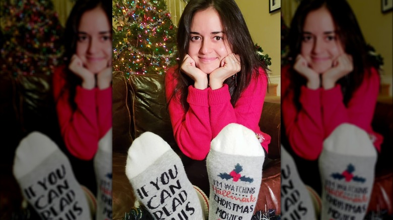 Danica McKellar poses for a selfie in front of her Christmas tree, wearing a red sweater and Christmas socks.