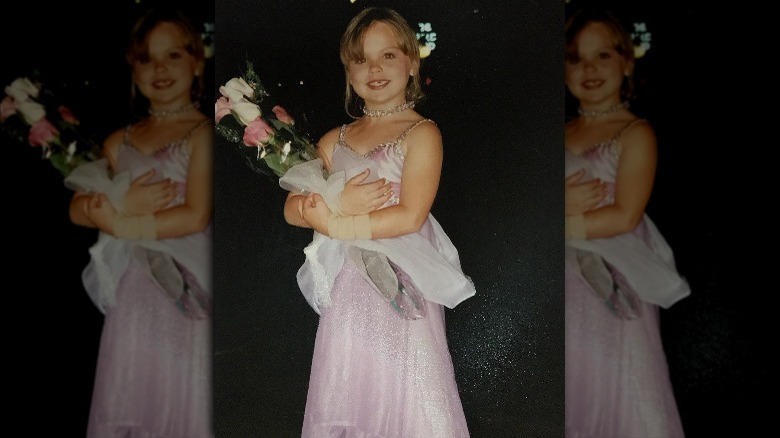 Hannah Brown as a child in a gown holding flowers.