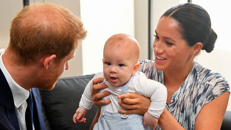 Meghan Markle holding her son, Archie, with Prince Harry looking at him.