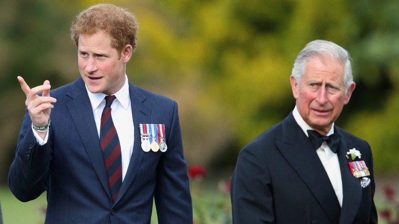 Prince Harry and Prince Charles at an outdoor event wearing suits and military medals