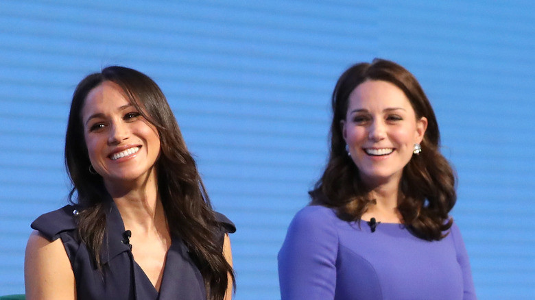 Meghan Markle and Kate Middleton smiling and looking to side