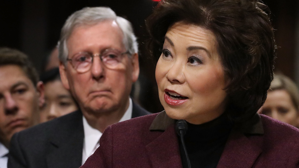 Elaine Chao speaks while Mitch McConnell sits behind her