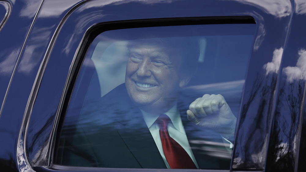 Donald Trump signaling to supporters with his fist from inside a car
