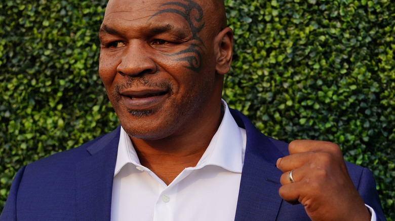 Mike Tyson raises his fist in front of a wall of leaves