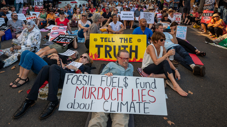 Protesters sitting/lying in the street with signs against Murdoch