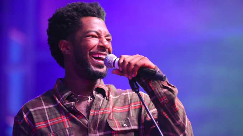 Willie Jones, singing into a microphone, 2019 concert, wearing a plaid shirt