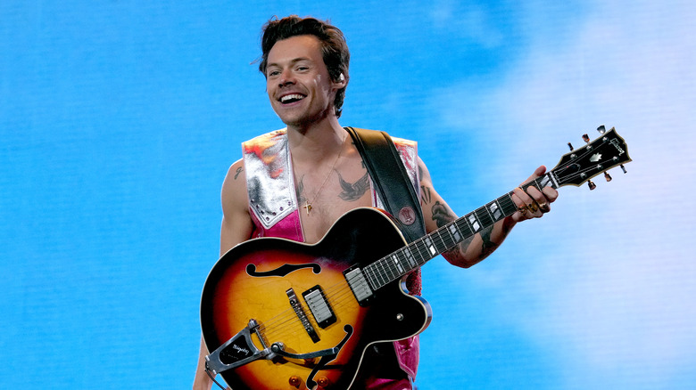 Harry Styles on stage holding a guitar and smiling