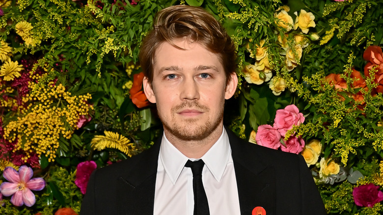 Joe Alwyn posing in front of a flower wall