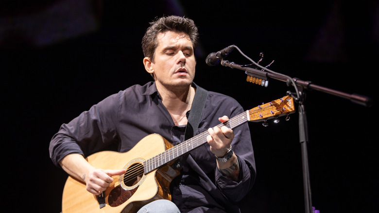 John Mayer on stage playing guitar in front of a microphone