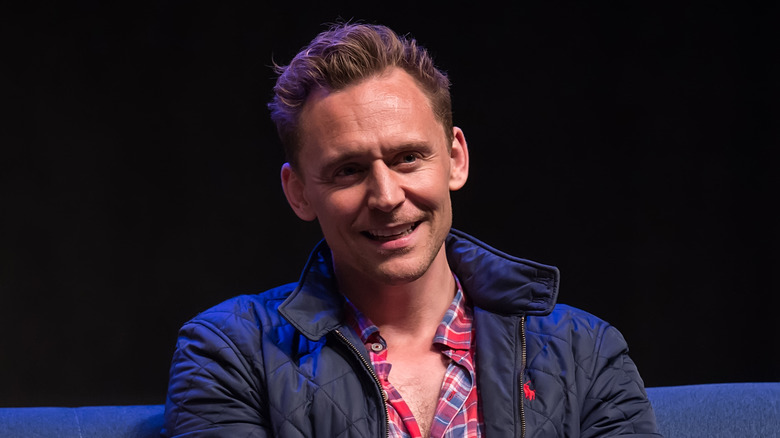 Tom Hiddleston smiling while seated on stage