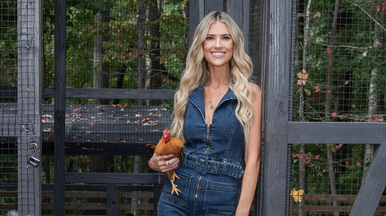 Christina Hall outside wearing denim and holding a chicken.