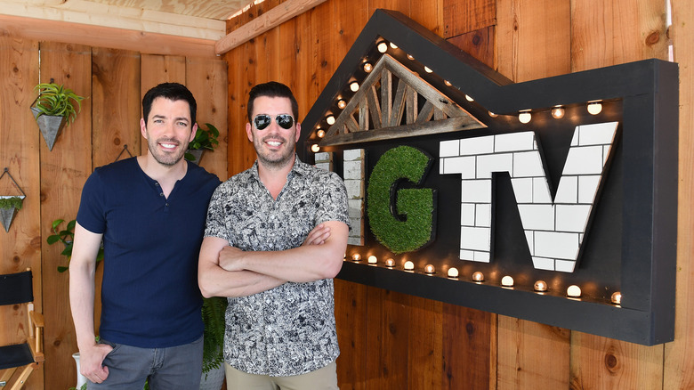 Drew Scott and Jonathan Scott posing beside HGTV sign