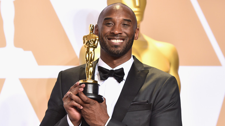 Kobe Bryant smiling and holding an Academy Award up