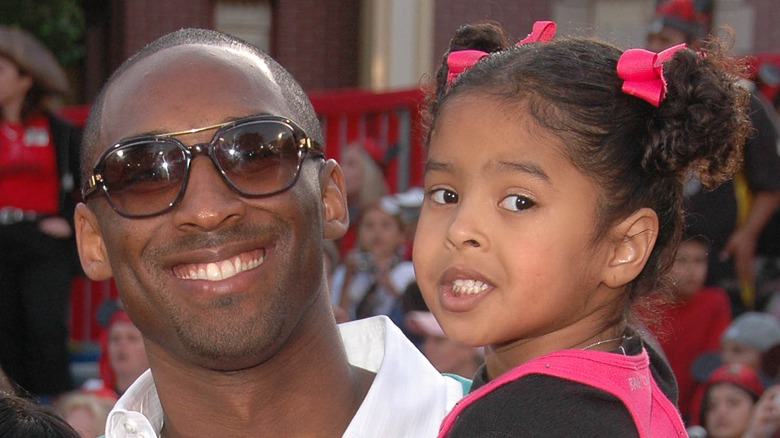 Kobe Bryant smiling in sunglasses while holding Natalia Bryant