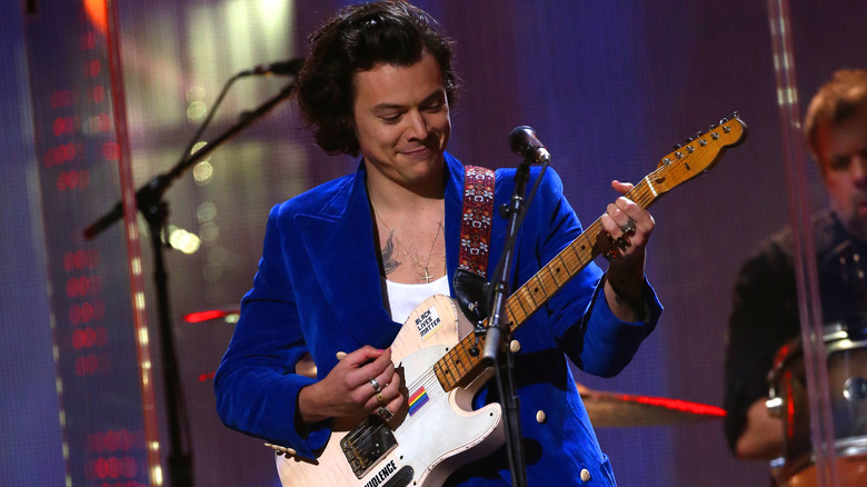 Harry Styles playing guitar in a Gucci blue suit