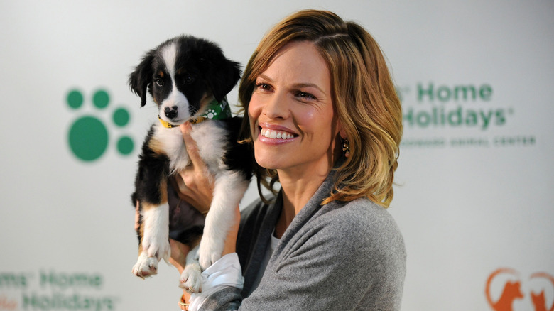 Hilary Swank smiles while holding a dog