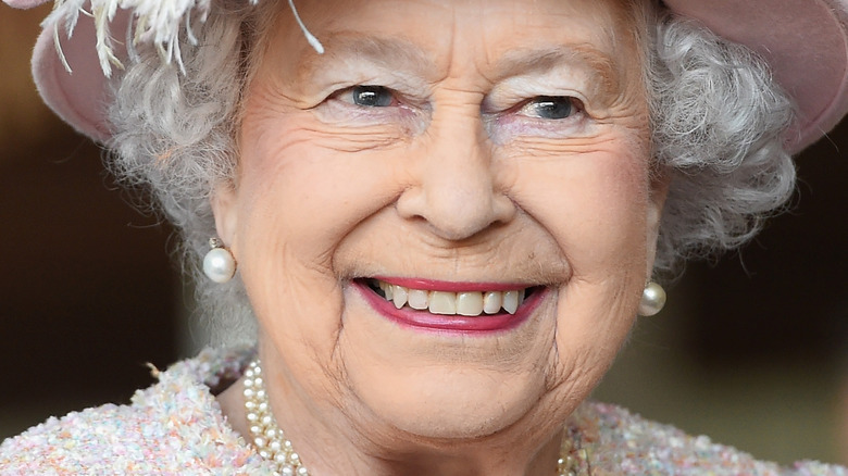 Queen Elizabeth II smiles in a pink hat