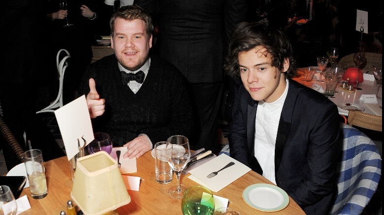 James Corden and Harry Styles seated at table wearing suits