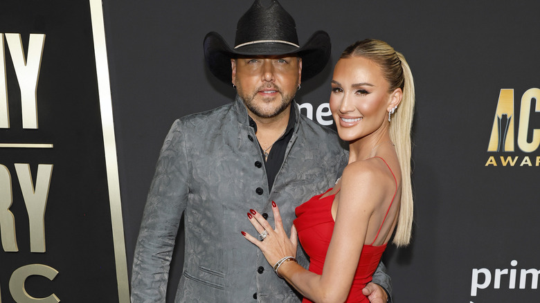 Jason Aldean standing with wife Brittany at red carpet event