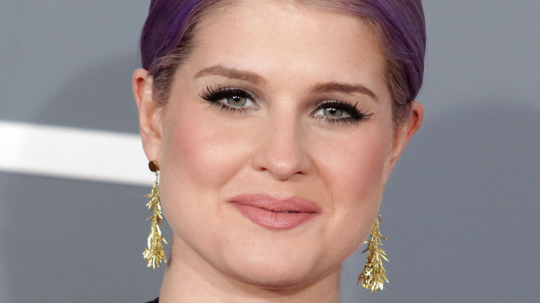 Kelly Osbourne wears gold dangly earrings while smiling