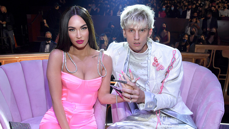 Megan Fox and Machine Gun Kelly sitting on a pink couch.