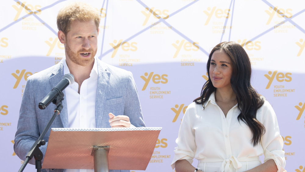 Prince Harry speaking at podium next to Meghan Markle 