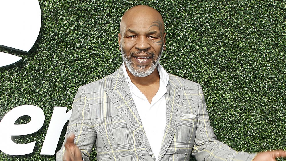 Mike Tyson posing in front of grassy wall in a checkered blazer