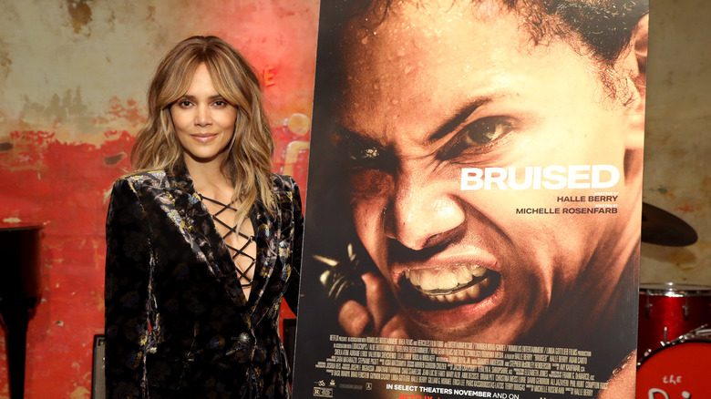 Halle Berry posing next to Bruised poster