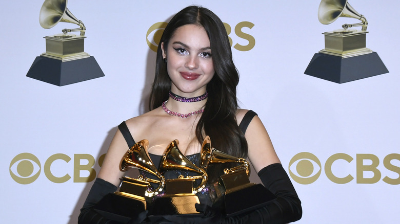 Olivia Rodrigo smiling and holding three Grammys