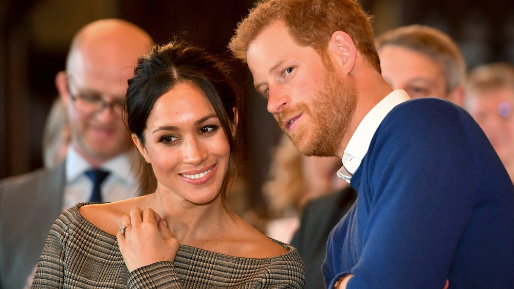 Meghan Markle laughs in a off shoulder top as Prince Harry whispers in her ear