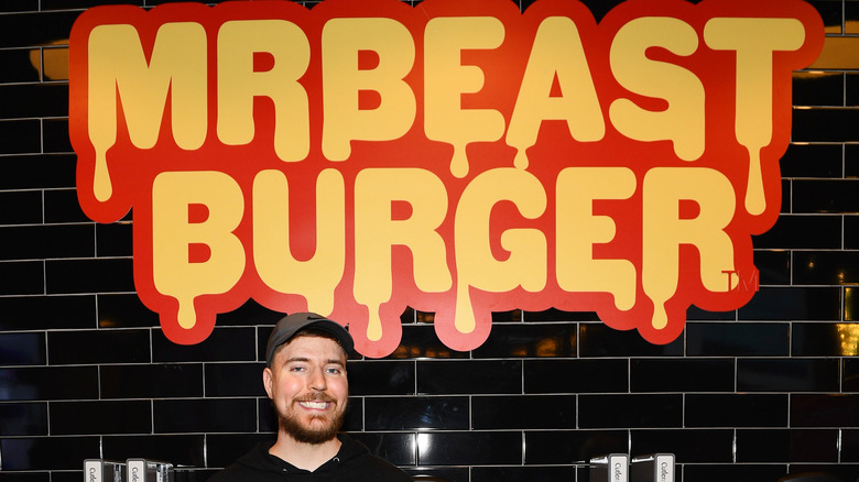 MrBeast standing by MrBeast Burger sign.