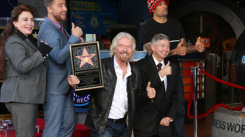 Richard Branson smiling and giving thumbs up holding his Hollywood star