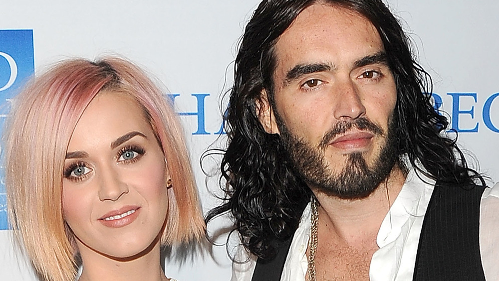 Katy Perry in a pink bob hairstyle posing next to Russell Brand who is wearing a black vest over a white button-up shirt