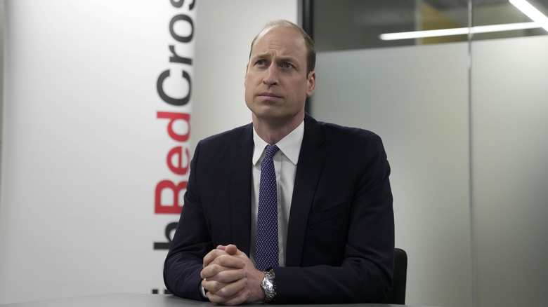 Prince William sitting at desk in black suit blue tie