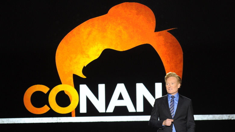 Conan O'Brien standing in front of his show's logo