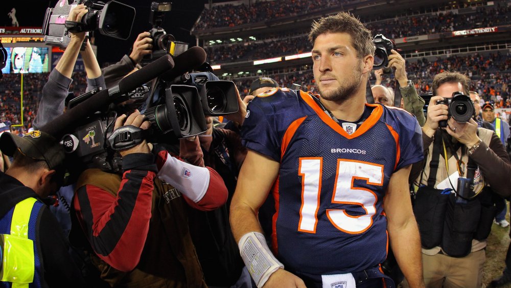 Tim Tebow in a Denver Broncos uniform, surrounded by reporters