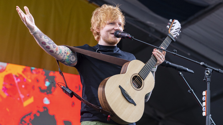 Ed Sheeran speaking into microphone with guitar in hand