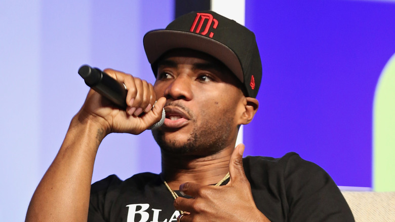 Charlamagne tha God wears a black baseball cap and black t-shirt while speaking into a microphone