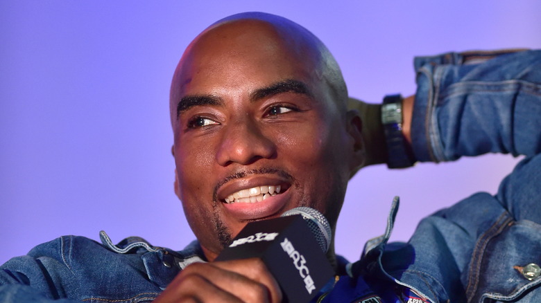 Charlamagne tha God wears a denim jacket and a wristwatch as he speaks into a microphone