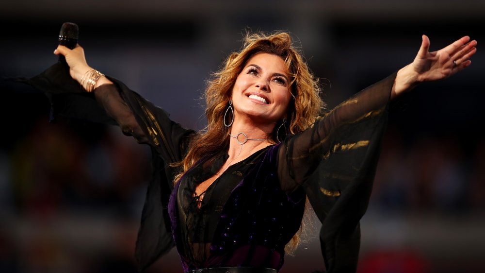 Shania Twain smiling on stage with her arms outstretched