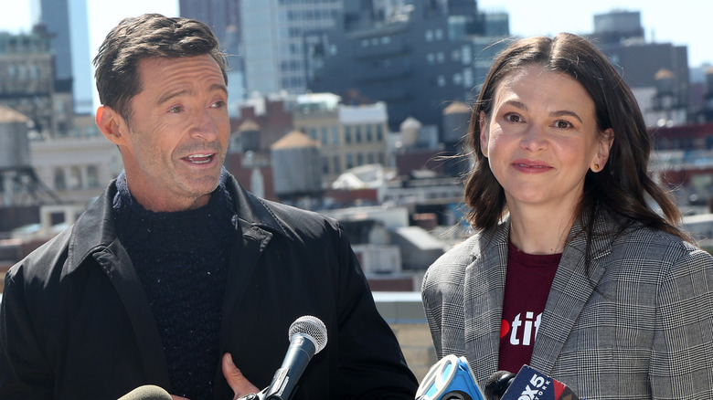 Hugh Jackman wearing a black jacket and blue turtleneck sweater with Sutton Foster wearing a grey plaid jacket and maroon t-shirt